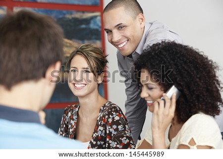 Smiling businesspeople listening to colleague in meeting while woman using cellphone