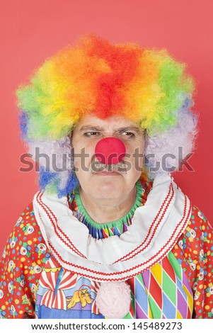 Senior male clown frowning over red background