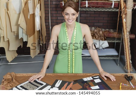 Portrait of beautiful female fashion designer standing at table with layouts