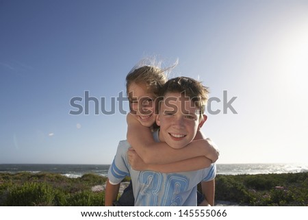 Portrait of young boy giving sister piggyback ride with ocean in background