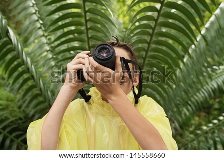 Young boy in raincoat taking photos in forest during field trip