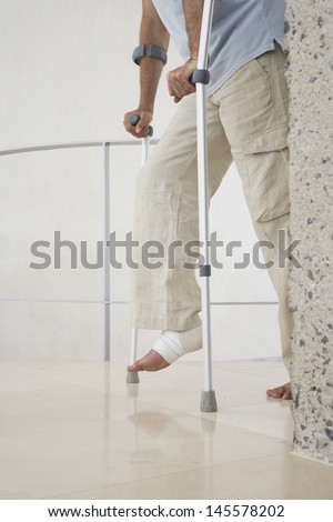Low section of man with broken leg walking with crutches at home