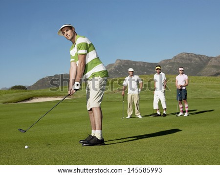 Full length of young male golfer playing golf with competitors in background