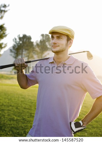Confident young male golfer holding club on golf course