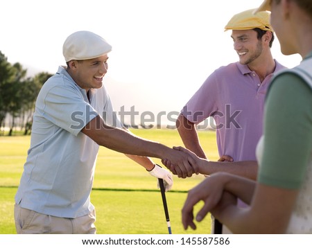 Cheerful young golfers shaking hands on golf course