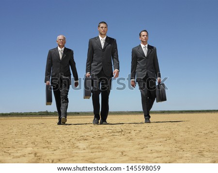 Full length of three businessmen with briefcases walking in desert