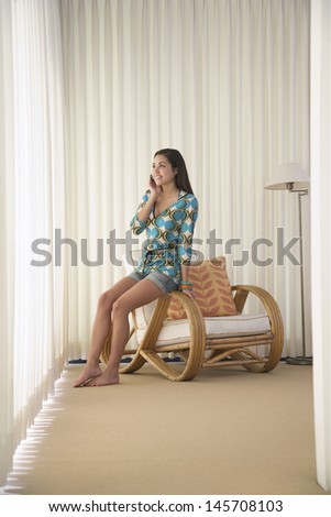 Full length of teenage girl using cell phone on armchair in corner of room