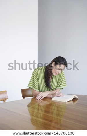 Beautiful young woman reading book at dining table