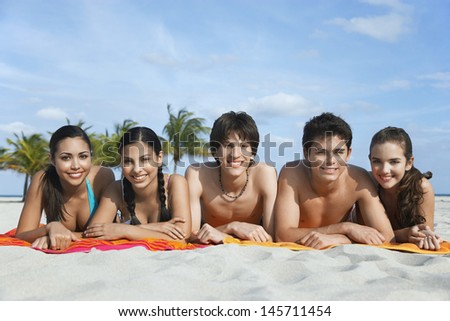 Portrait of happy teenage friends lying in row on beach towels