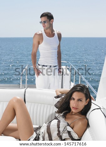 Portrait of sensuous young woman lying on sofa with man standing in yacht