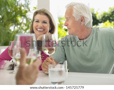 Happy middle aged couple having wine with friend at verandah table
