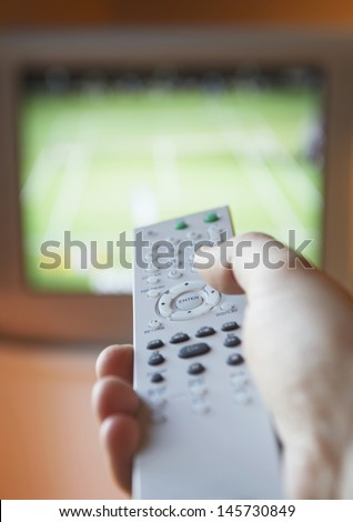 Closeup of female hand using remote control in front of TV