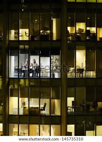 Business meeting viewed through illuminated window of office block at night