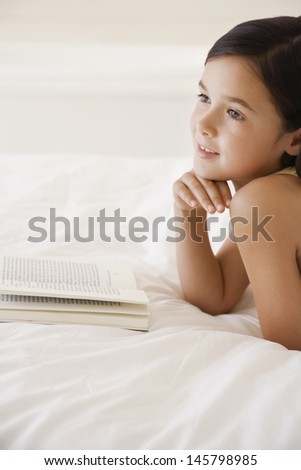 Happy little girl daydreaming while reading story book in bed