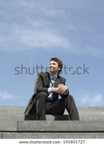 Low angle view of happy young businessman sitting on steps against sky