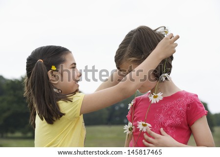 Cute little girl giving friend daisy chain in meadow