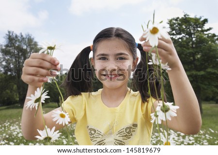 Portrait of happy young girl holding daisy chains in meadow