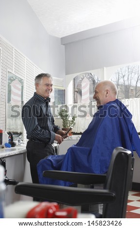 Side view of happy senior male barber and customer in hair salon