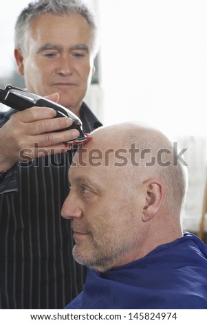 Hairdresser shaving male customer\'s head with hair trimmer in barbershop