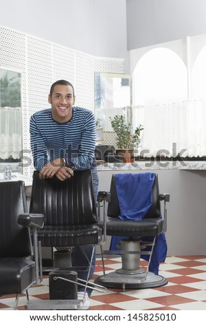 Portrait of happy young man leaning on chair in hair salon