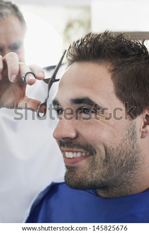 Closeup of happy man getting an haircut from hairdresser in barber shop