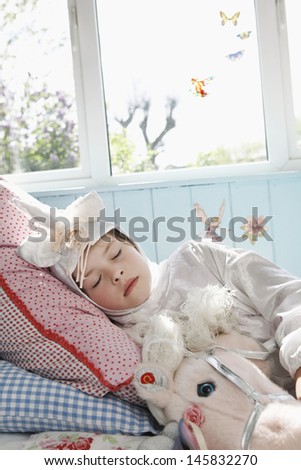 Young girl in unicorn costume sleeping in bed with toy horse