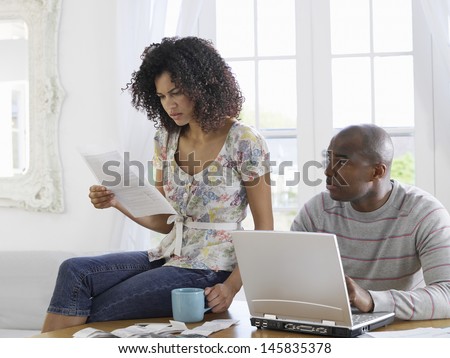 African American couple sitting at table using laptop and reading document