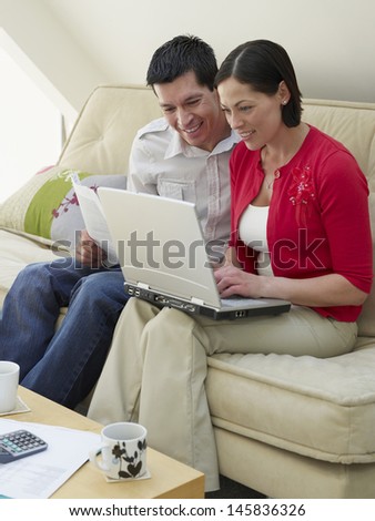 Smiling young couple sitting at sofa with laptop and bills