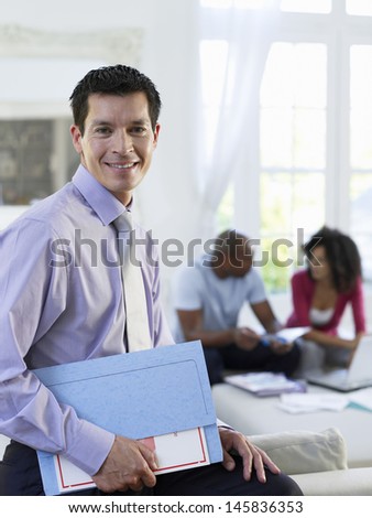 Portrait of a financial consultant holding folder with couple sitting in background