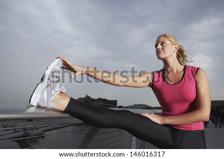 Side view of a young woman stretching on foot bridge