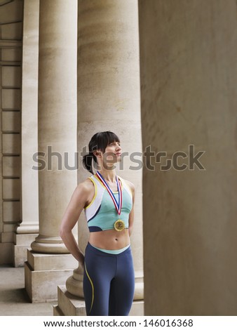 Confident female athlete wearing gold medal and standing in portico