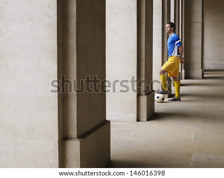 Full length side view of a soccer player holding foot on ball in portico
