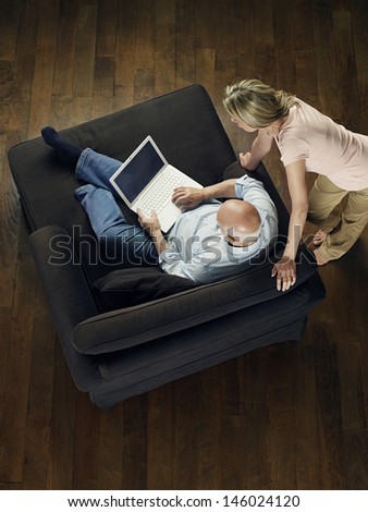 Top view of a woman watching mature bald man use laptop on sofa at home