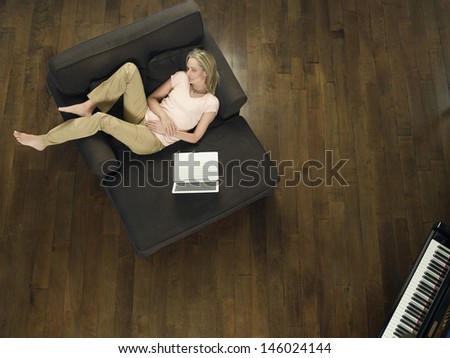 Top view of a middle aged woman with laptop sleeping on sofa in living room