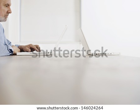 Side view of a mature man using laptop by another laptop at desk