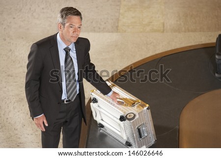 Serious businessman with suitcase at luggage carousel in airport