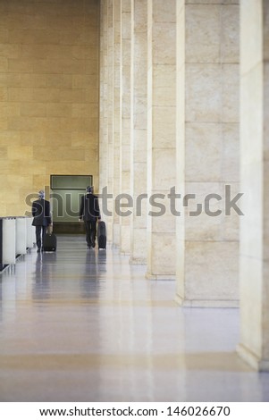 Full length rear view of two businessmen pulling luggage in airport lobby