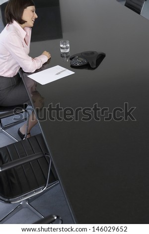 Side view of a happy young businesswoman with calculator and document at conference table