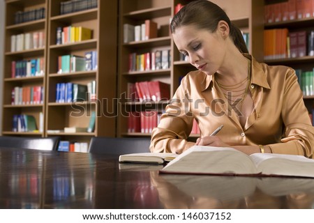 Beautiful young woman studying at desk in library