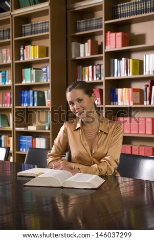 Portrait of a smiling young woman with book at desk in library