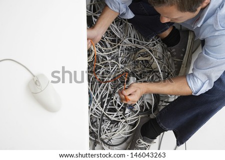 Closeup of a cropped man working on tangled computer wires in office