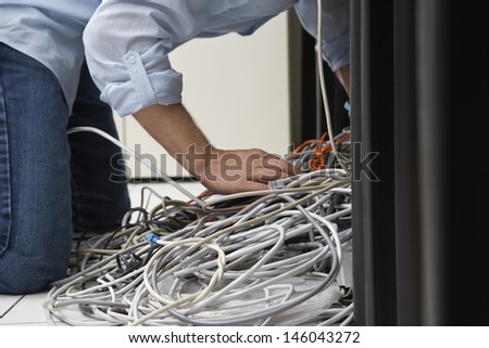 Side view of a man working on tangled computer wires in office