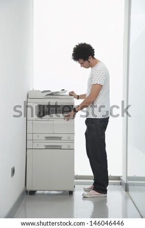 Full length side view of a young man using copy machine in office hallway