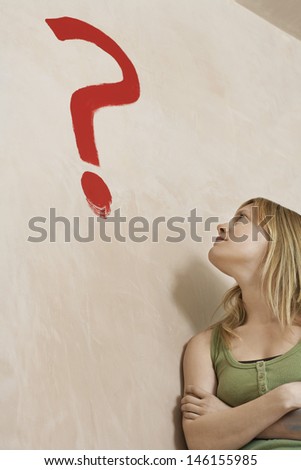 Young blond woman leaning against wall with painted question mark over head