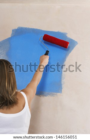 Rear view of a woman painting wall blue with paint roller
