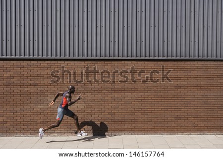 Side view of an African American man running by brick wall