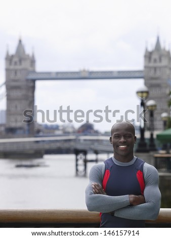 Portrait of a smiling young African American man with arms crossed in front of Tower Bridge in England