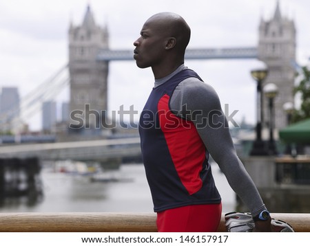 Side view of an African American man stretching in front of Tower Bridge in England