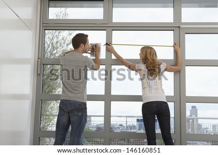 Rear view of young couple measuring window in modern apartment