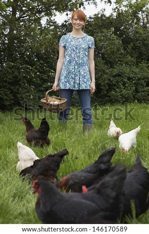 Portrait of a smiling young woman holding egg basket by hens in the garden